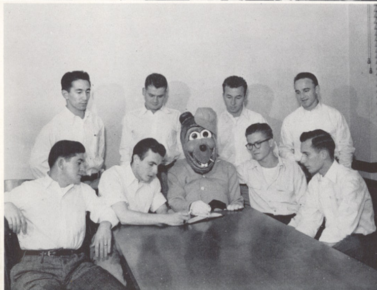 Archival scan: Oski seated with a group around a table. Photo credit: Photographer/artist uncredited in supplied scan.