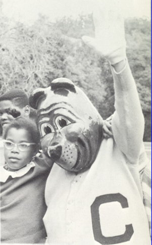 Archival scan: Oski waving beside a child outdoors. Photo credit: Photographer/artist uncredited in supplied scan.